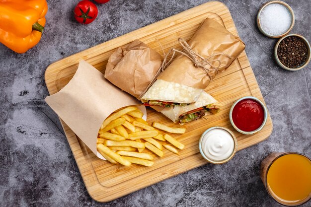Top view of beef burrito with tomato cucumber lettuce jalapeno served with fries and sauces