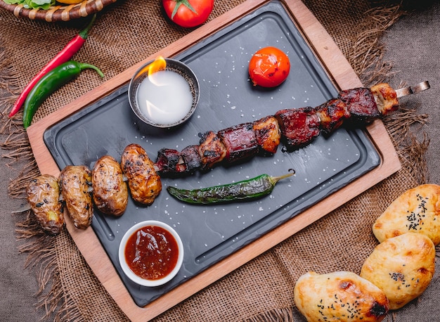 Top view beef liver kebab on a skewer with potatoes and tomato with grilled green pepper and sauce on a tray