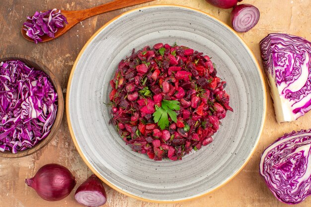 Top view beet salad dressed with parsley on a plate made of red onions chopped cabbage and other fresh veggetables on a wooden background