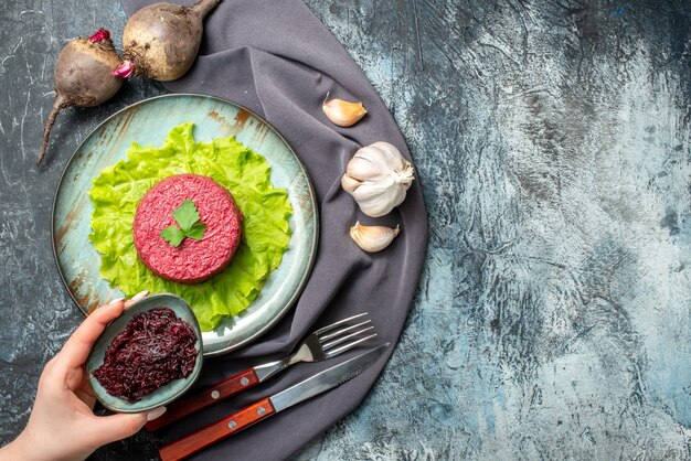 Top view beet salad on plate garlic beets grated beet in small bowl in female hand hand purple shawl on grey table