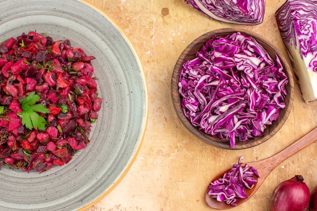 Вид сверху салат из свеклы на тарелке с красным луком и нарезанной красной капустой в миске на деревянном столе