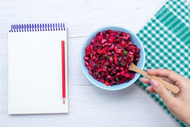 top view of beet salad sliced with greens inside blue plate with notepad on white desk, salad vegetable vitamine food meal health