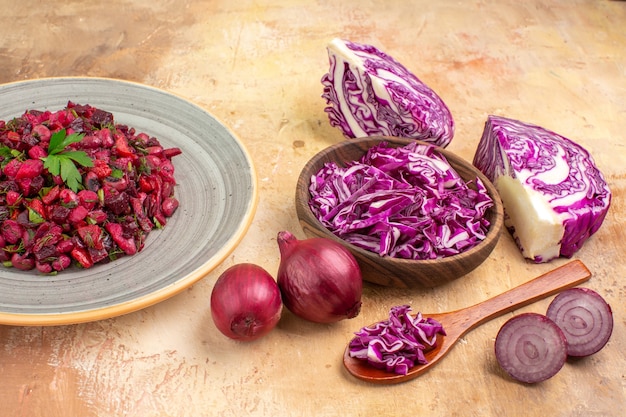 Top view beetroot salad on a ceramic plate with red onions and a bowl of chopped red cabbage on a wooden background