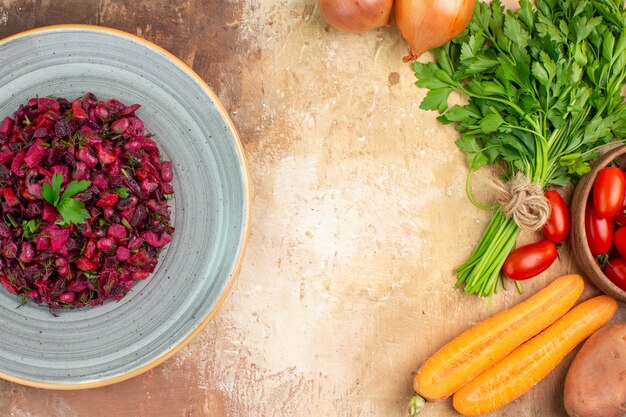 Top view beetroot salad mixed with parsley leaves on a ceramic plate with vegetables for its preparation on a wooden background with copy space