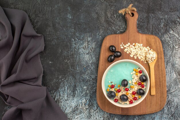 Top view of berries oatmeal grapes spoon on the board next to the dark tablecloth