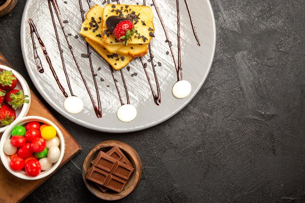 まな板の上のチョコレート菓子とイチゴのボウルの横にあるケーキチョコレートとイチゴのトップビューベリープレート