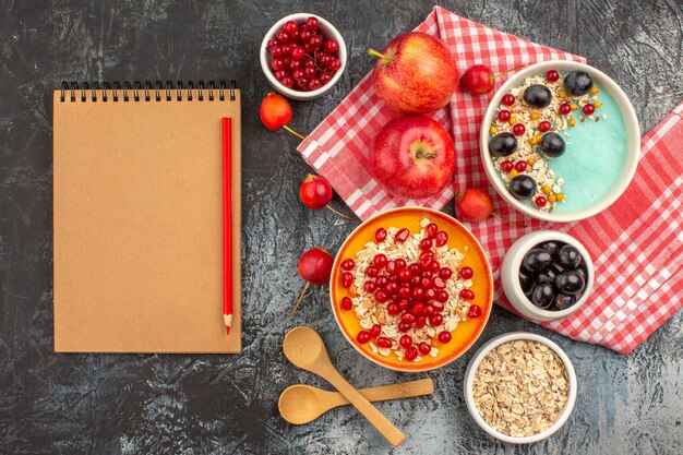 Top view of berries spoons apples colorful berries oatmeal pomegranate notebook