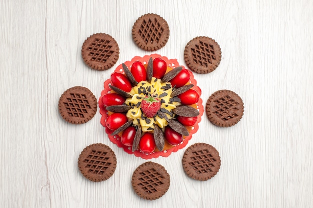 Top view berry cake on the red oval lace doily and cookies on the white wooden table