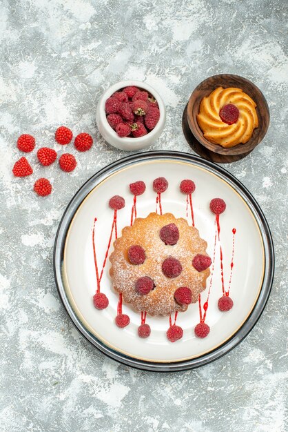 Top view berry cake on white oval plate biscuit bowl with raspberries on grey surface