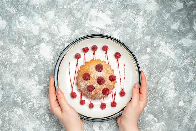 Torta di bacche vista dall'alto sul piatto ovale bianco in mano femminile su spazio libero superficie grigia