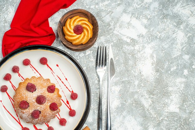 Top view berry cake on white oval plate red shawl biscuit fork and dinner knife on grey surface copy space