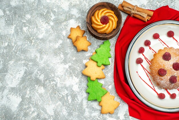 Top view berry cake on white oval plate red shawl cinamon cookies on grey surface copy space