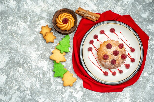 Top view berry cake on white oval plate red shawl cinnamon sticks cookies on grey surface