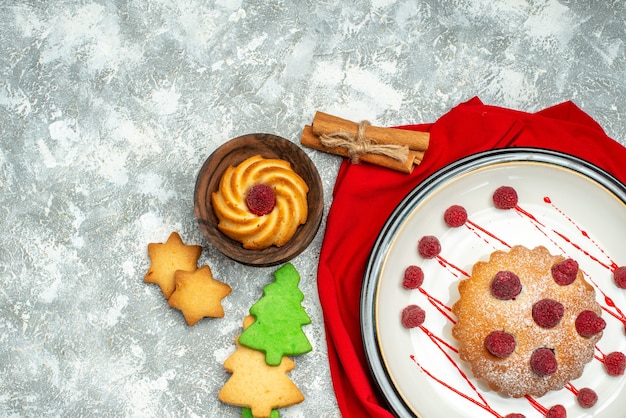 Foto gratuita torta di bacche di vista superiore sul piatto ovale bianco biscotti dell'albero di natale dello scialle rosso su spazio libero di superficie grigia
