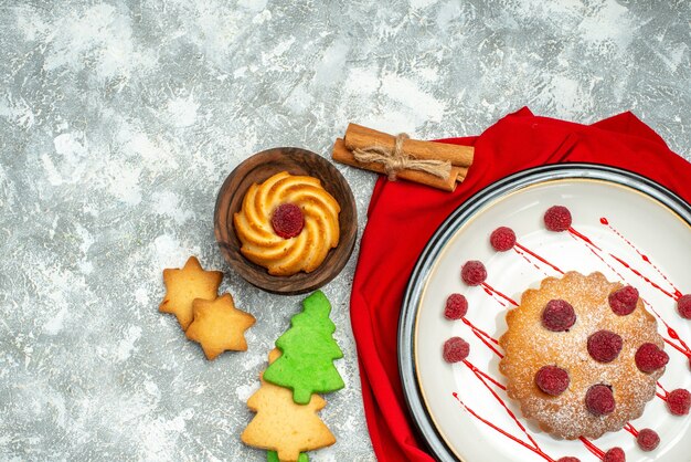 Top view berry cake on white oval plate red shawl xmas tree cookies on grey surface free space