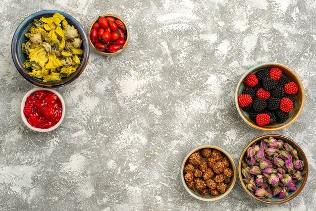 Вид сверху ягодные конфитюры с орехами и сухоцветами на белом фоне конфитюр, конфеты, чай, сладкий