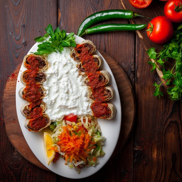 Top view beyti kebab with yogurt and parsley and salad in white plate