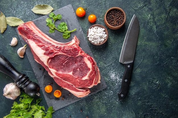 Top view big meat slice raw meat with pepper and greens on dark surface