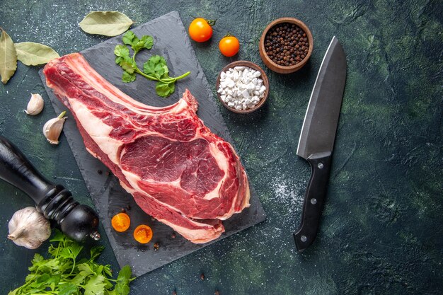 Вид сверху большой кусок мяса сырое мясо с перцем и зеленью на темной поверхности