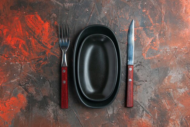 Top view big small plates fork and knife on dark red background