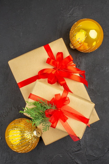 Top view big and small xmas gifts in brown paper tied with red ribbon balls on dark surface