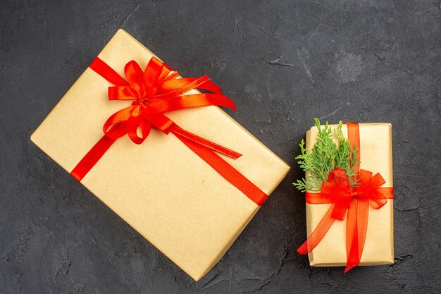 Top view big and small xmas gifts in brown paper tied with red ribbon branch fir on dark surface