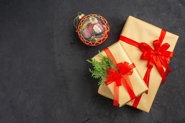 Top view big and small xmas gifts in brown paper tied with red ribbon xmas ball on dark background free place