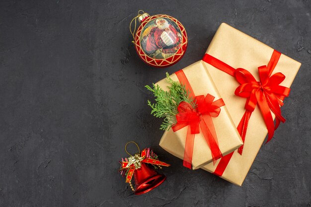Вид сверху большие и маленькие рождественские подарки в коричневой бумаге, перевязанные красной лентой, елочные игрушки на темном фоне