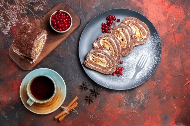 Top view of biscuit roll with cup of tea on dark surface