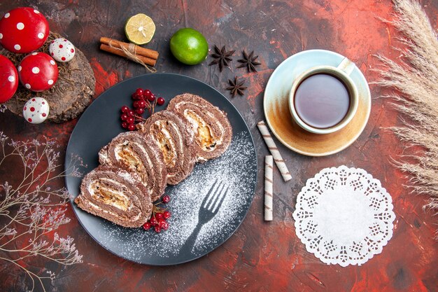 Top view of biscuit rolls with cup of tea on dark surface