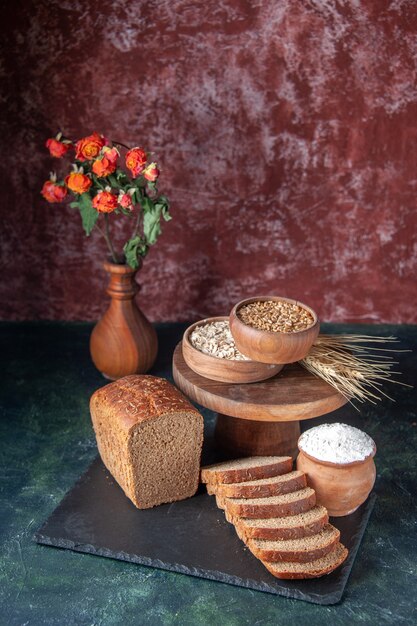 Top view of black bread slices on black tray and flour in brown bowl on maroon background