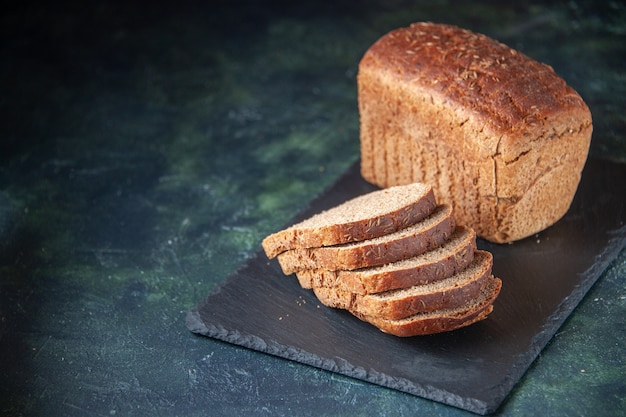 Top view of black bread slices on black wooden tray on the left side on blue color distressed background