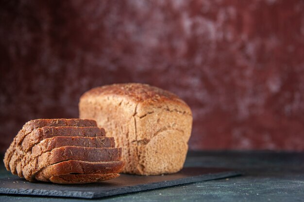 Top view of black bread slices on black wooden tray on the right side on mixed colors distressed background