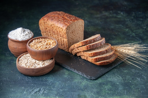 Free photo top view of black bread slices flour oatmeal buckwheat on dark color board on blue distressed background