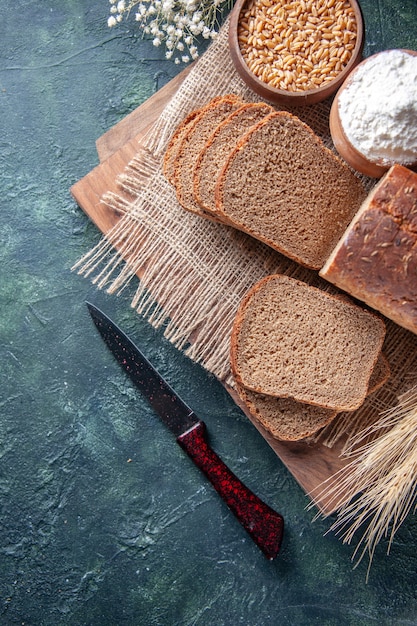 Top view of black bread slices flour wheat on nude color towel spikes flower on cutting boards on mixed colors background