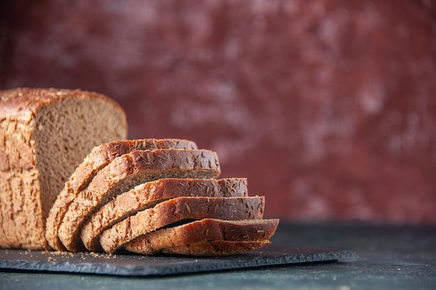 Free photo top view of black bread slices knife on dark color board on maroon distressed background