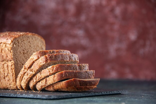 Top view of black bread slices knife on dark color board on maroon distressed background