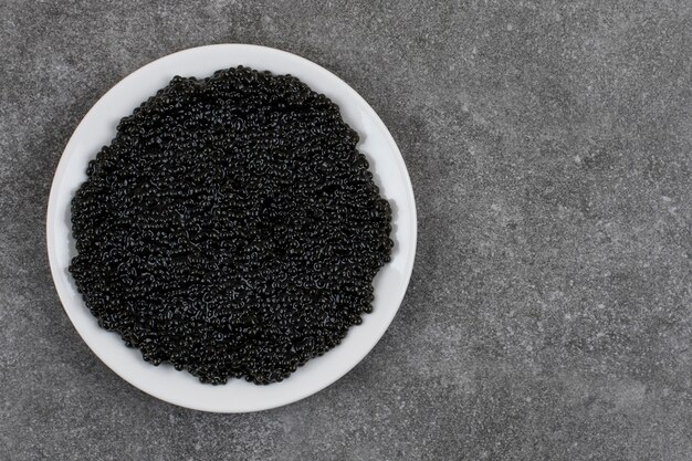 Top view of black caviar on white plate over grey surface