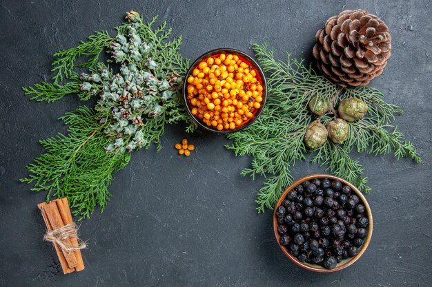 Top view black currant sea buckthorn in bowls pine branches cinnamon sticks on dark surface