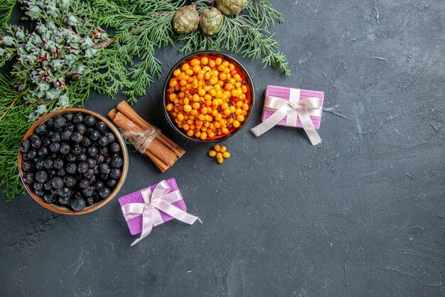 Top view black currant sea buckthorn in bowls pine branches on dark surface free space