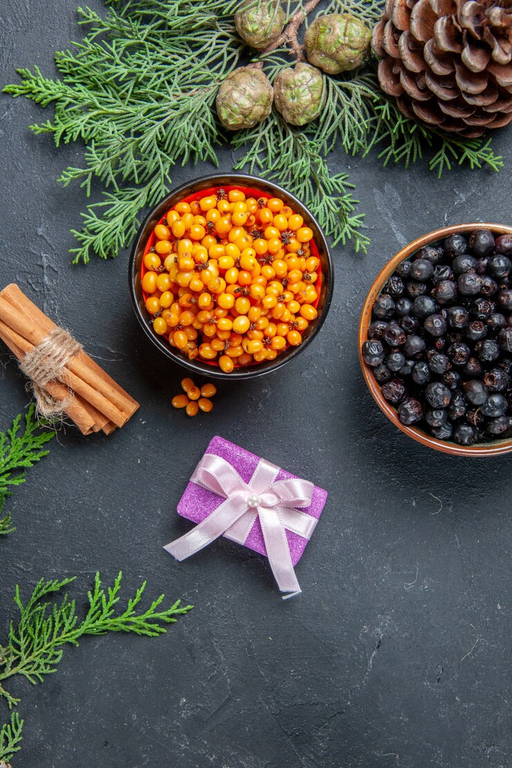 Free Photo top view black currant sea buckthorn in bowls pine branches pinecones cinnamon on dark surface