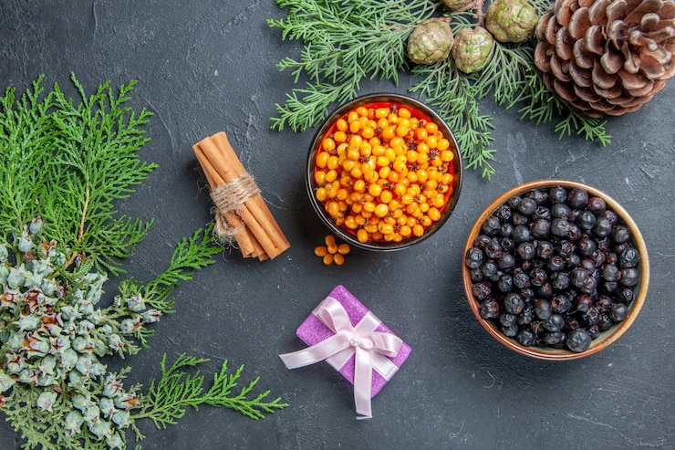 Free Photo top view black currant sea buckthorn in bowls pine branches pinecones on dark surface