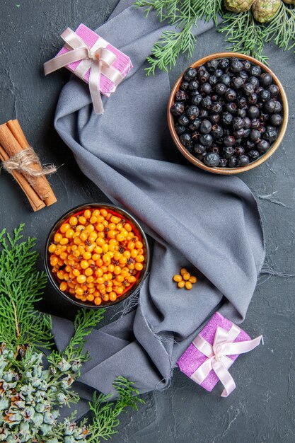Top view black currant sea buckthorn in bowls pine branches purple shawl small gifts on dark surface