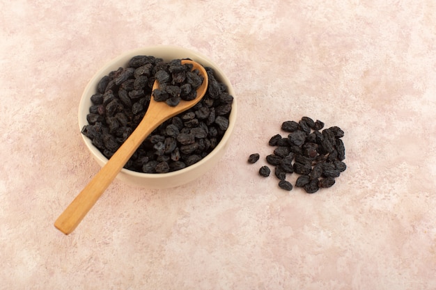 A top view black dried fruits inside round plate with wooden spoon on pink