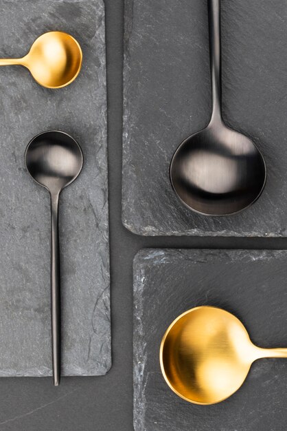 Top view of black and golden spoons on slate