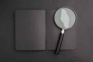 Free photo top view black notebook magnifying glass on dark table