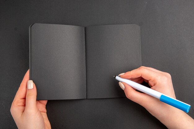 Top view black notepad and pen in female hands on black table