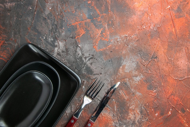 Top view of black oval and rectangular platters fork and knife on dark red surface