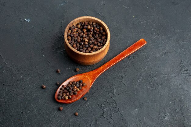 Top view black pepper bowl wooden spoon on black surface