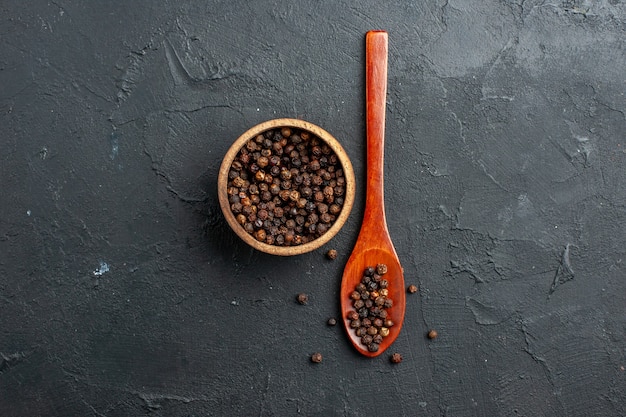 Top view black pepper bowl wooden spoon on dark surface copy place